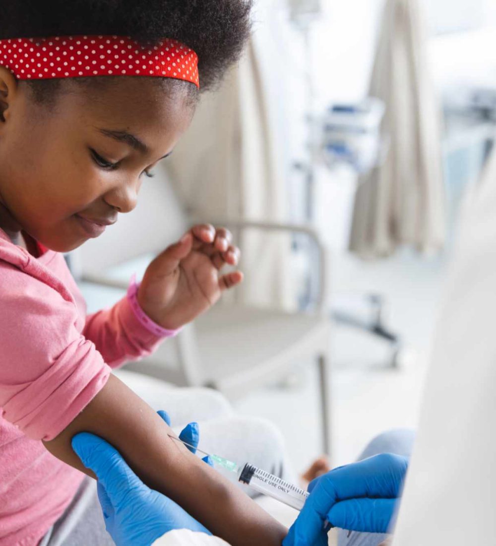 African american female doctor wearing face mask vaccinating girl patient at hospital. Hospital, hygiene, medicine and healthcare, unaltered.