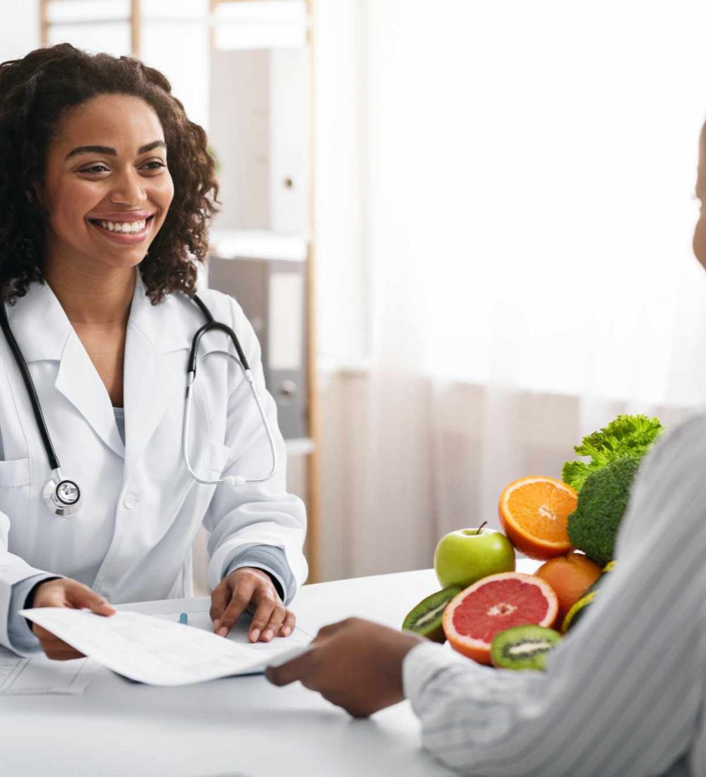 Personal diet. Cheerful african american female dietologist giving diet plan to woman client, clinic interior