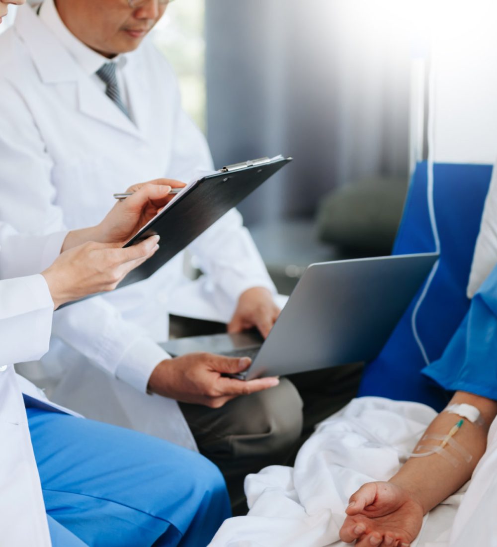 Two doctors talking to a patient lying in his bed  with receiving saline solution in hospital